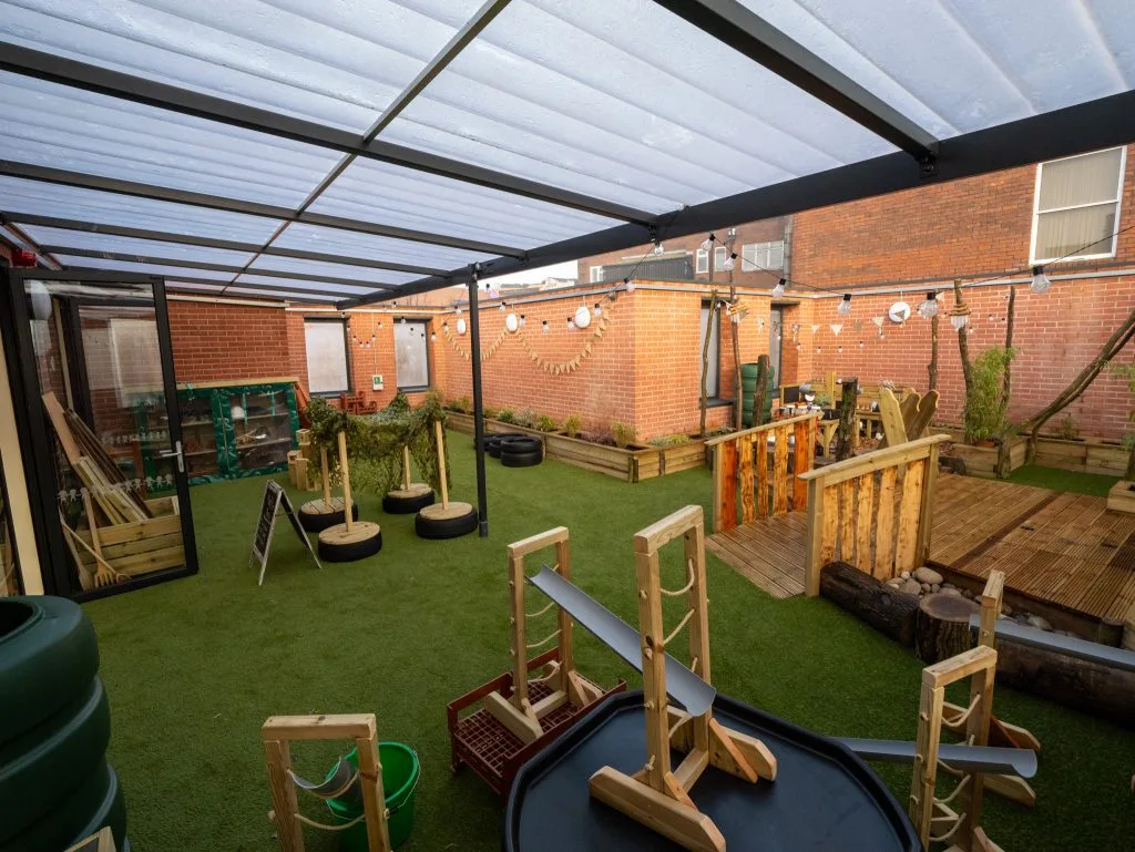 Covered outdoor play garden at Kids Planet Stanley Square with wooden climbing frames, artificial grass and brick walls